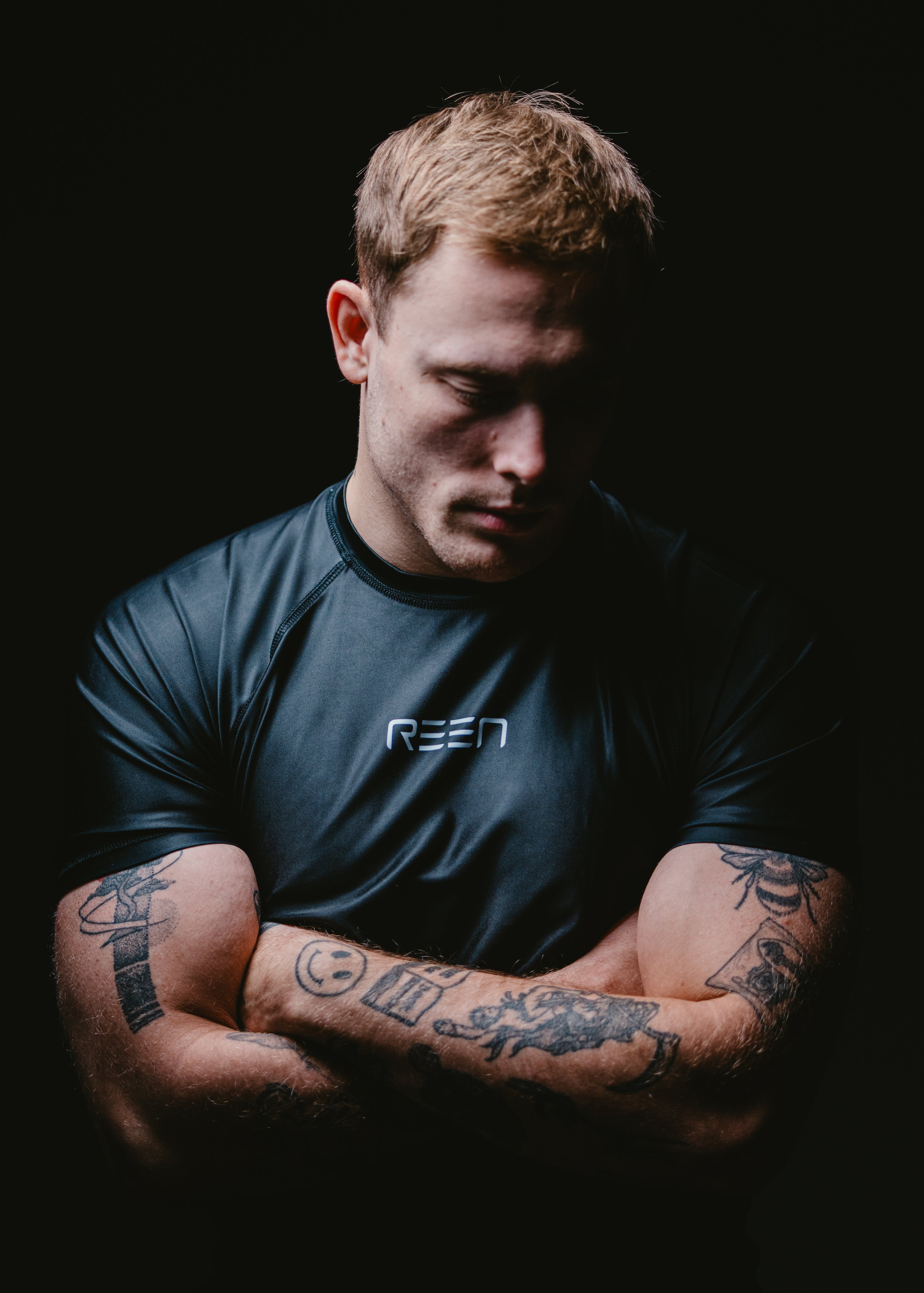 Man wearing a black t-shirt with a brand logo, standing against a dark background